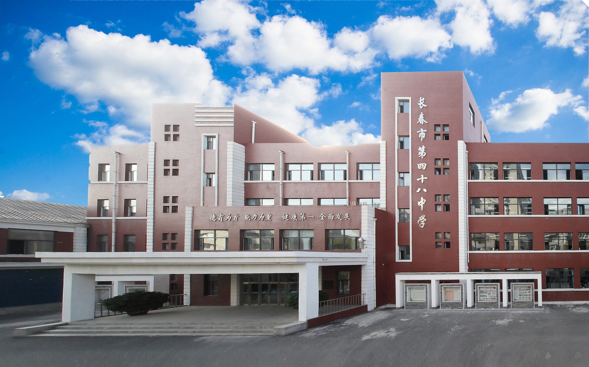 长春市第四十八中学教学楼全景，红褐色校舍前设有主入口，背景为蓝天白云