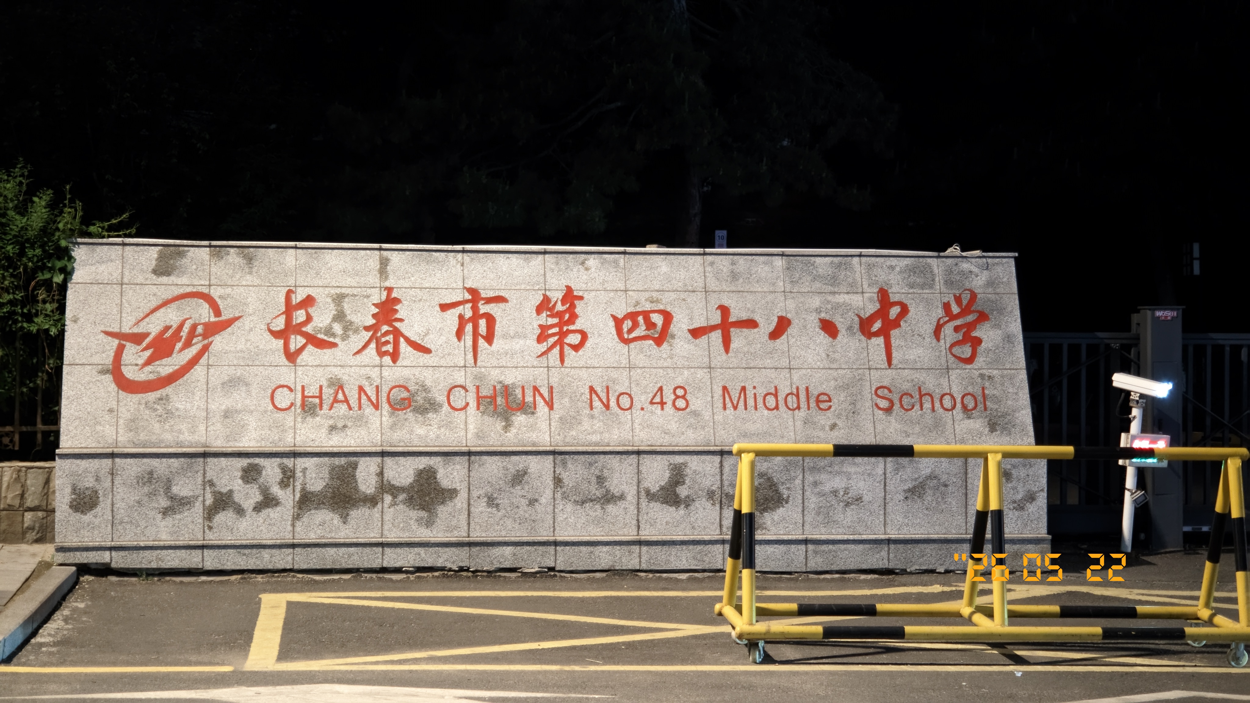 夜间灯光下的长春市第四十八中学校名墙，灰色石墙上有红色中文校名和英文名称